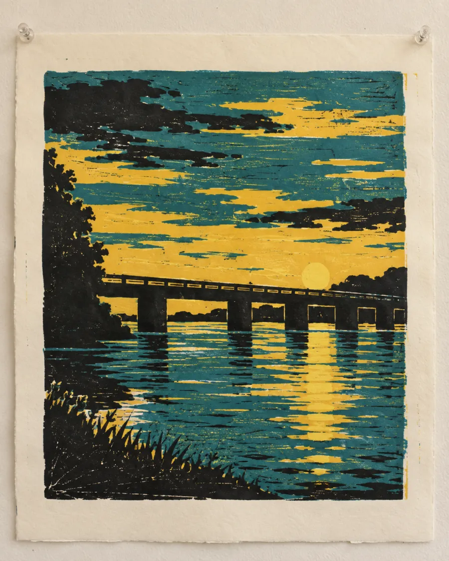 A three-colour linocut in yellow, teal and black of a long low bridge over a river at sunset