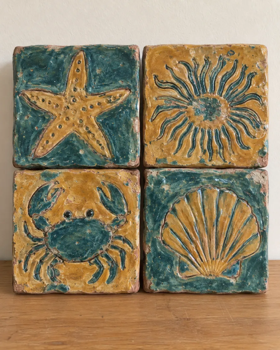 Four carved clay tiles showing a starfish, an anemone, a crab and a scallop shell, glazed teal and ochre